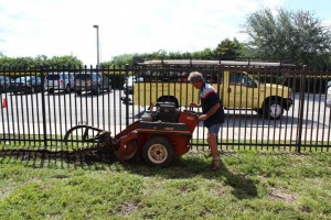 A man is using an electric powered machine to cut grass.