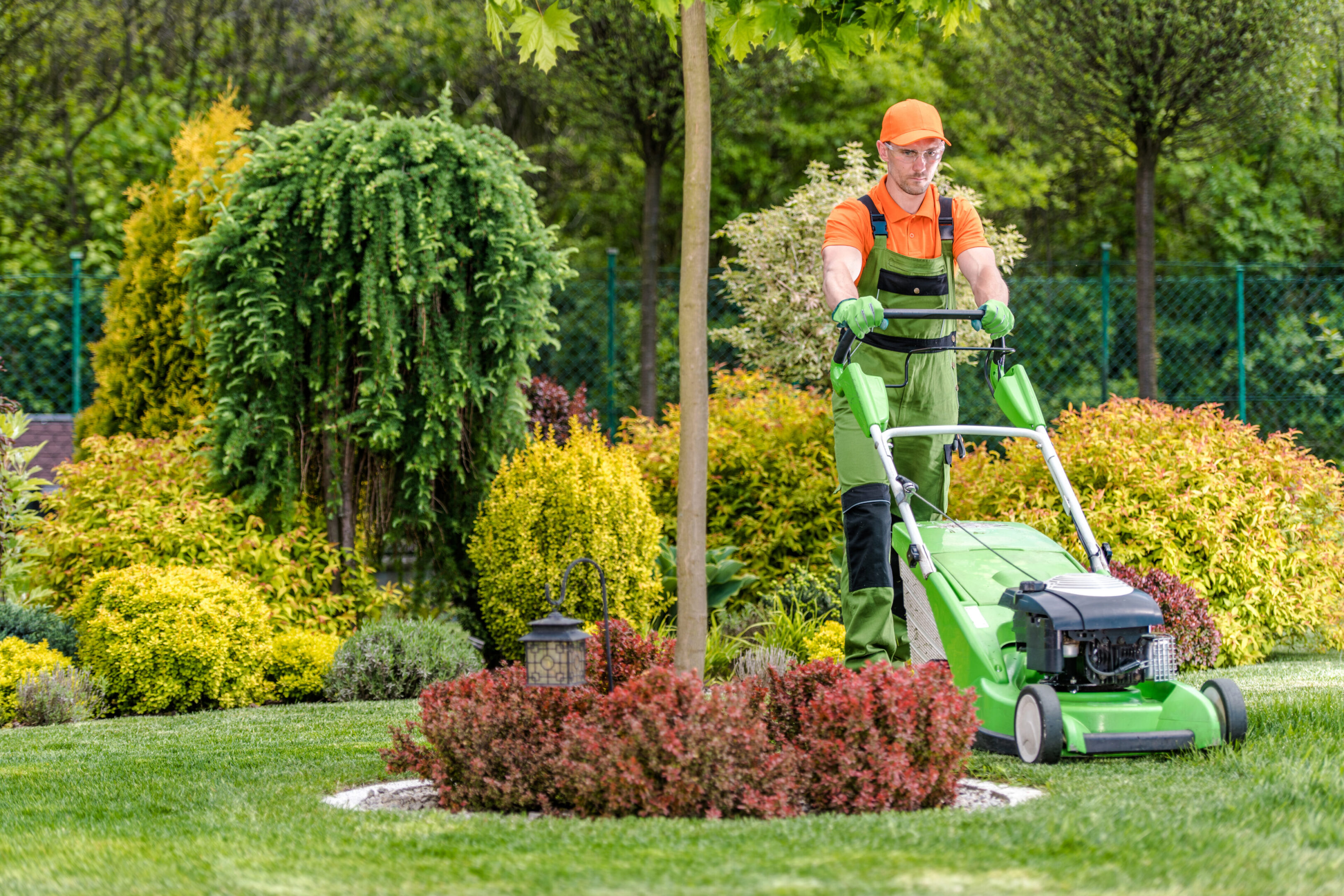Gardener mowing the lawn in a vibrant garden with flowers and trees.