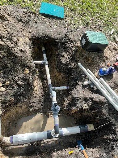 Exposed plumbing pipes and connectors in a muddy ground area.