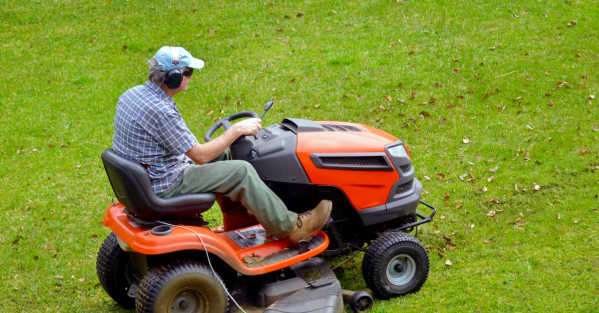 Person riding a bright orange lawn mower on green grass.